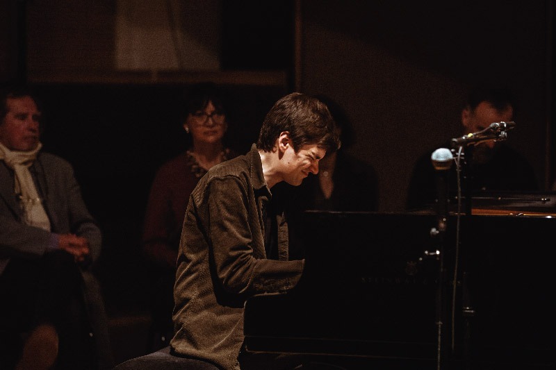 Vue de côté de Bram De Looze jouant du piano avec une grande concentration.