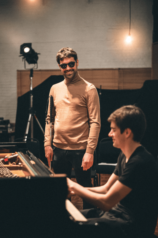 Bram De Looze plays the piano and Karl Meesters stands next to him