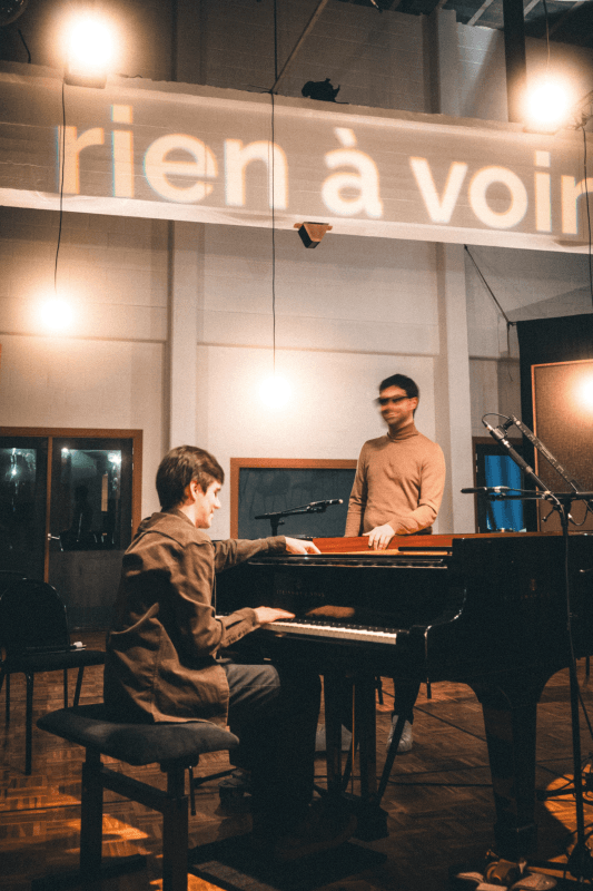 Bram De Looze joue du piano et Karl Meesters se tient à côté de lui.