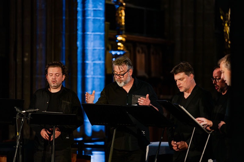 5 van de leden van vocaal ensemble Dionysos Now! Centraal geeft de dirigent de maat aan.