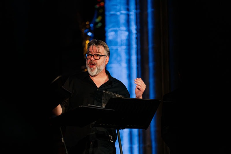 Close-up van tenor Tore Tom Denys tijdens zijn optreden met Dionysos Now!. Achter hem de blauw verlichte zuilen van de kerk.