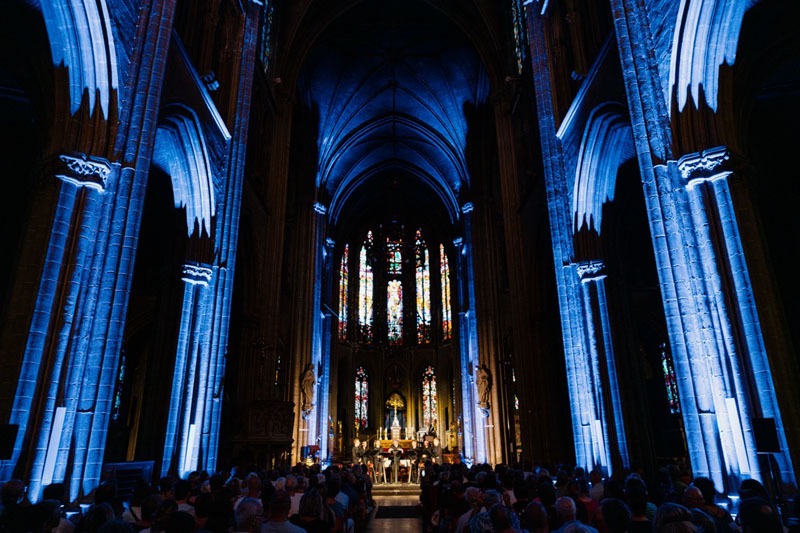 Zicht naar het altaar waar de zangers van Dionysos Now! staan. In de kerk is het donker, de constructie is met blauwe lampen verlicht.