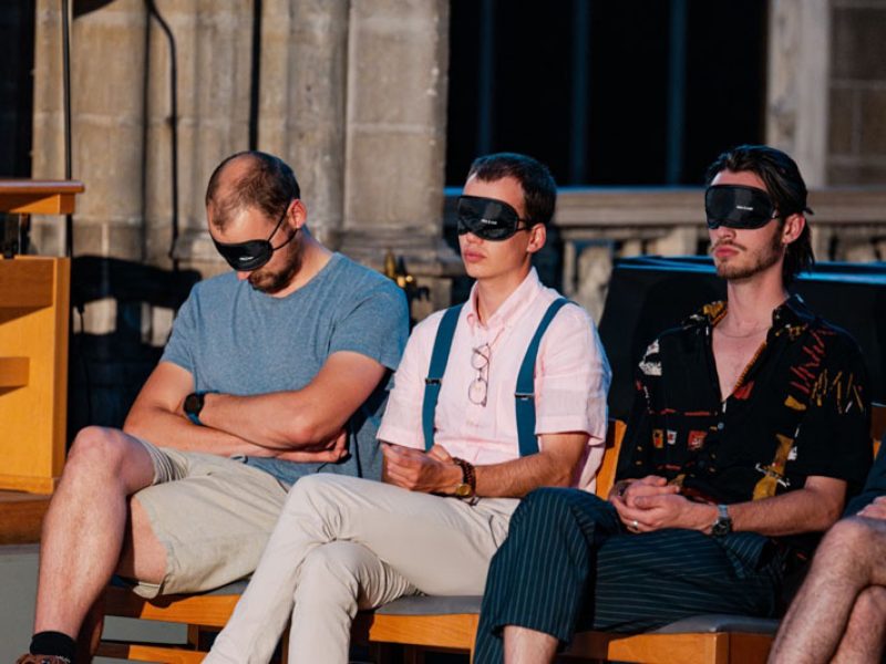 Dans l'église, 3 personnes assises avec un masque pour les yeux écoutent le concert de Dionysos Now!
