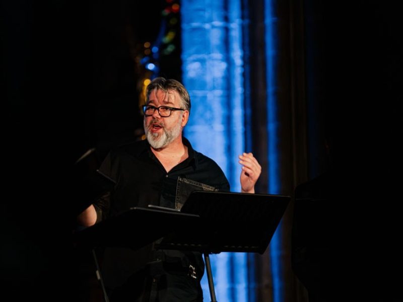 Gros plan du ténor Tore Tom Denys lors de sa prestation avec Dionysos Now! Derrière lui, les colonnes de l'église éclairées en bleu.